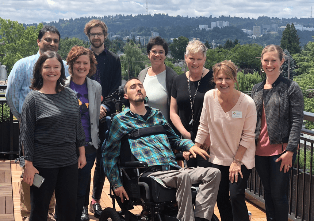 Nine people pose for a photo on a roof deck with trees and buildings on the hill in the background