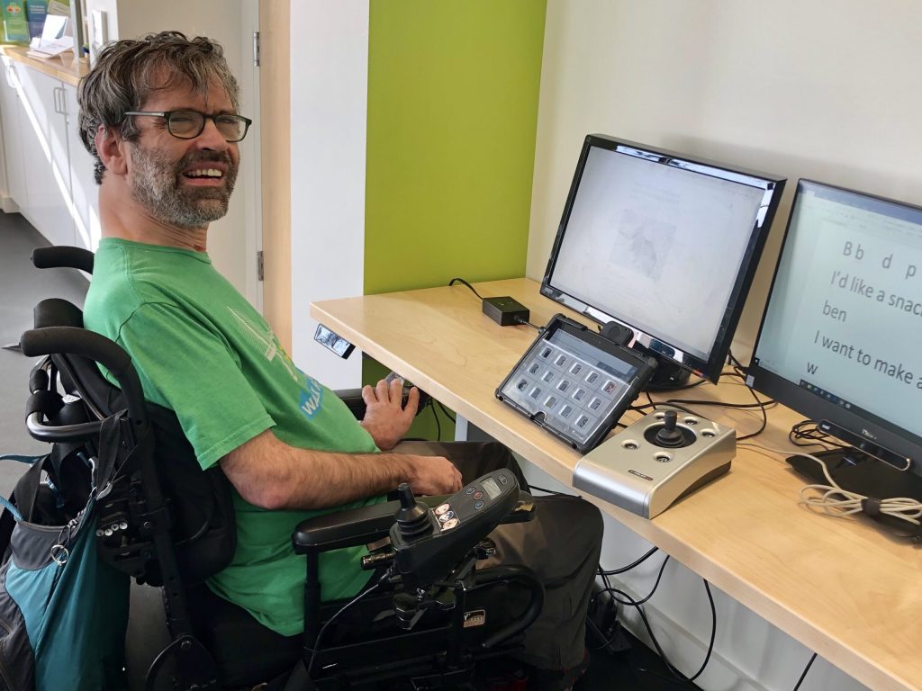 Man in green shirt tries out keyguard on speech generating device