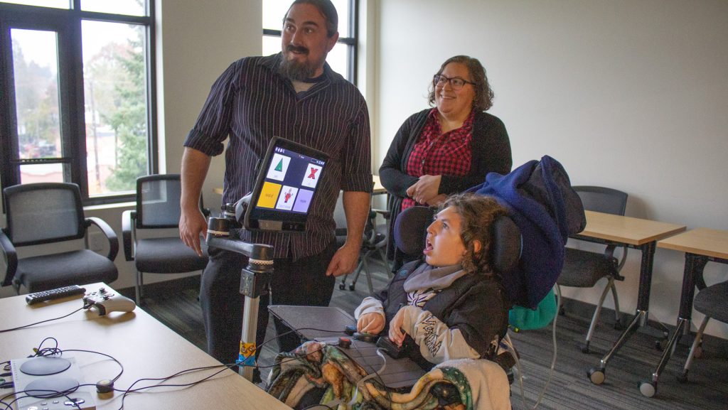 a child plays video games with an adaptive controller while their parents look on