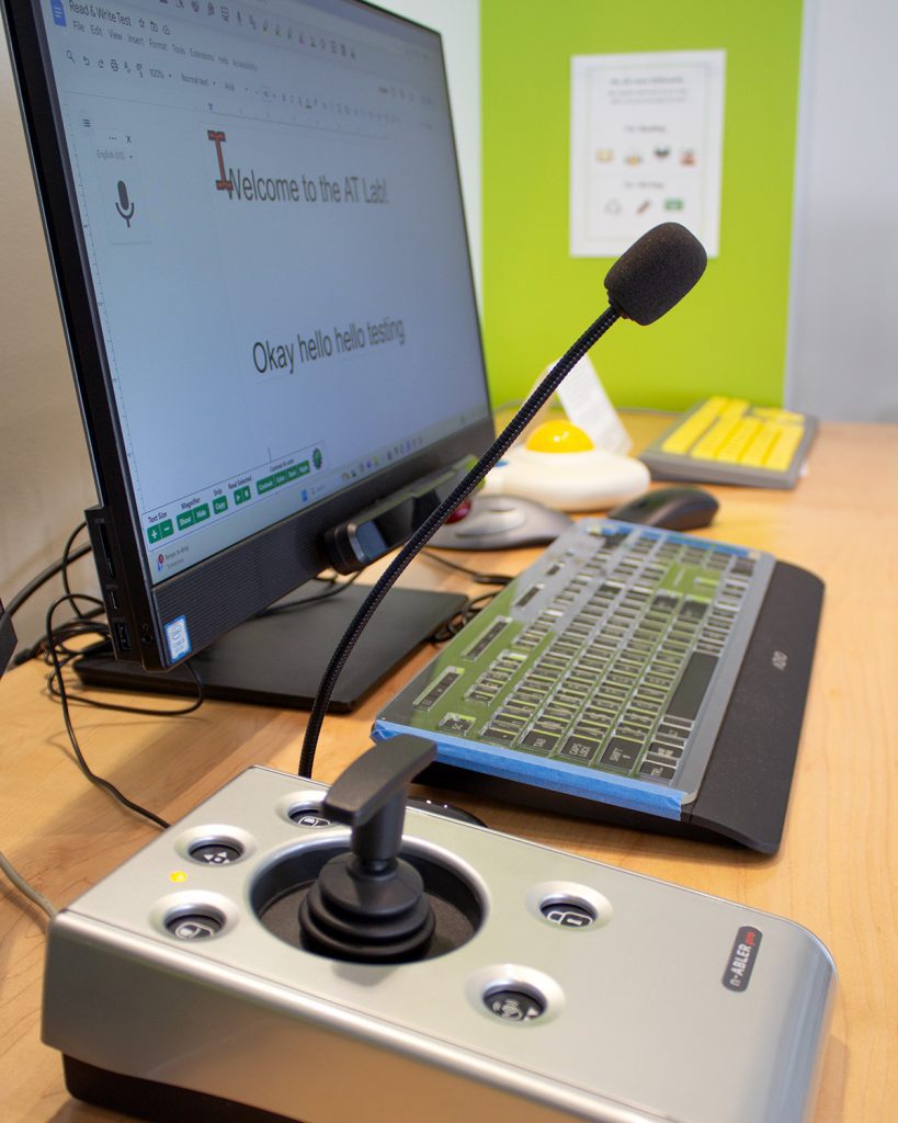 examples of assistive technology tools for using a computer, including a joystick, microphone, key guard on keyboard, and an adaptive mouse