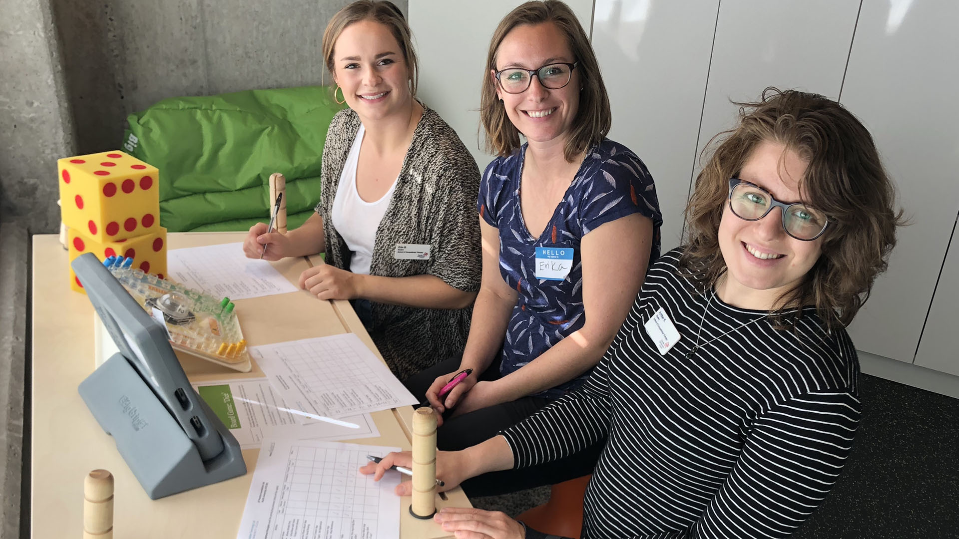 three smiling women wearing nametags sit together and work on worksheets