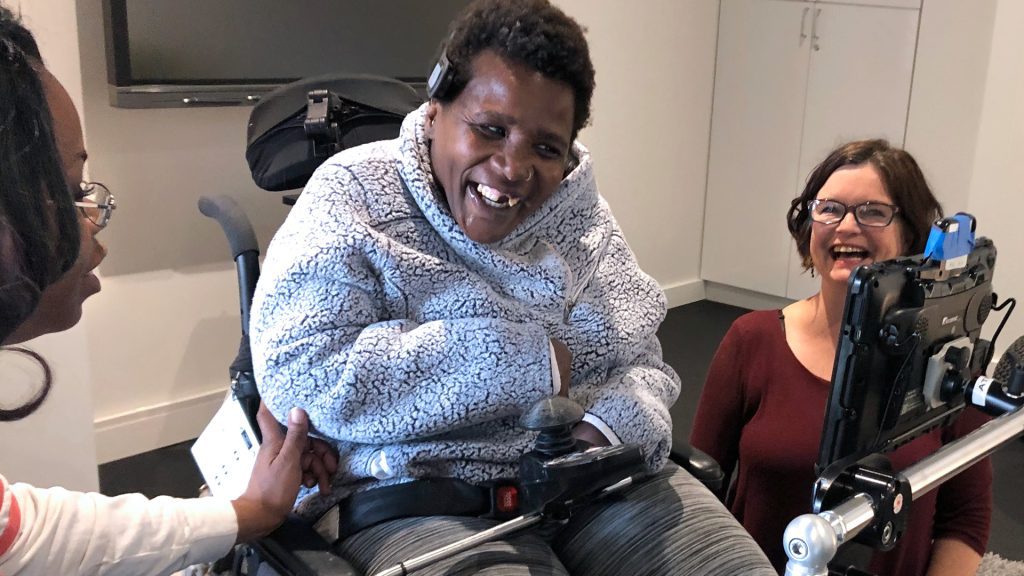 Woman who uses AAC and a wheelchair at a consultation with her support person and an SLP